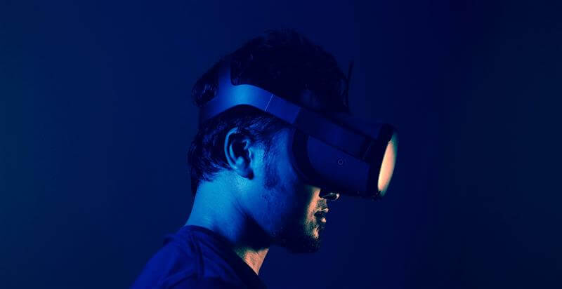 A man wearing a VR headset stands against a solid blue background, immersed in a virtual experience.